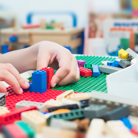 Image of white hands building colored LEGO blocks