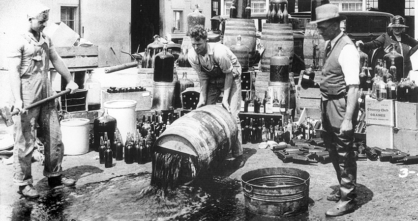 historical photo of three men dumping barrels of alcohol