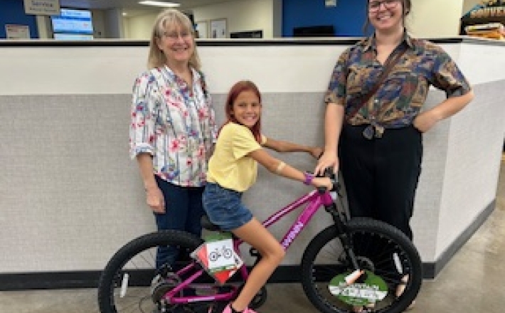 Girl on pink bike with library staff 